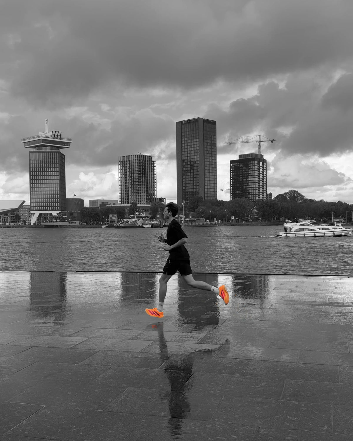 A runner with orange shoes crosses a wet quay on the IJ in Amsterdam, black and white